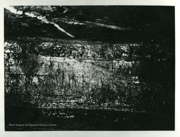 'All White Oak mines work the same seam of coal, viz: Sewall...The face of one of the working places or rooms is shown in this picture. The coal averages about 48 to 50 inches in thickness. This working place is now ready to be cut by the undercutting machine, so it can be shot down by the miner and loaded into the cars for transportations to the tipple. The white line on the roof in this picture is the center line of the room set by the engineers to guide the men operating the mining machine in driving the room straight.'