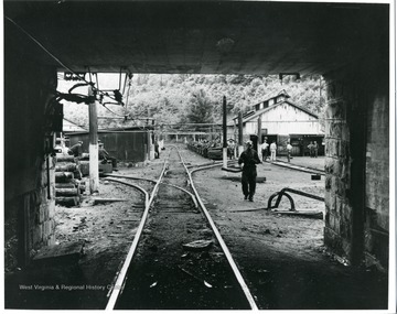 Miner entering the entrance to the mine.  Cars loaded with miners in the background.