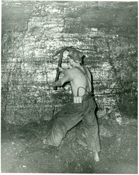 Miner working on a wall in a coal mine with a pick axe.