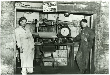 Two miners at work. A sign above their heads reads 'No Loafing Allowed'.