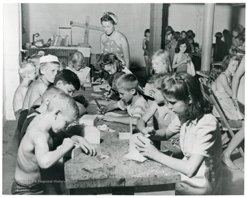 Children make crafts while older people watch over them.