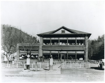 Three men stand outside of the building, while others are inside. There are two Esso gas pumps in front of the building.