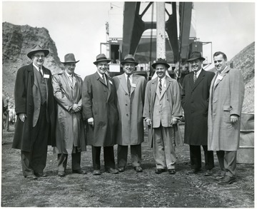 Group portrait of men standing in front of large shovel.