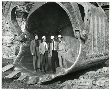 Group portrait of men standing in giant scoop.