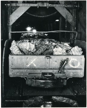 'This is an end view of one of our new steel mine cars on a cage at one of the White Oak Shaft mines, and the signal has just been given to hoist it to the surface, 450 feet up! These electric equipped hoists can hoist a car every twenty seconds and dump it! The cars are placed on the cages and automatically by creeper chains and car stops. One man operates the signals and car stops and chains.'