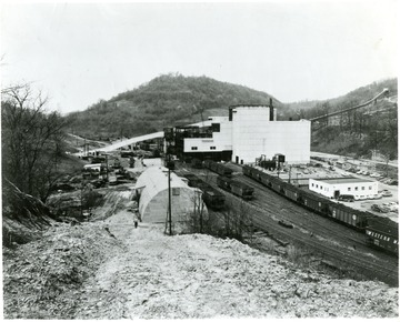 Lots of cars parked out front as well as filled coal cars coming out of the plant.