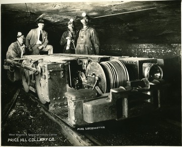 Miners and a man in a suit pose for a portrait with a mine locomotive.