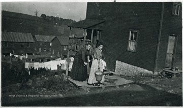 One woman pumping water from a well and one holding a bucket.