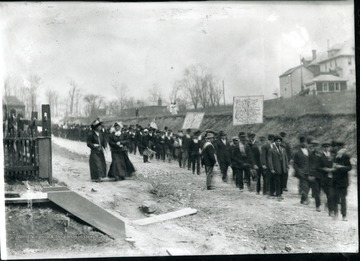 Miners carry signs and American flags while marching. One sign says 'We don't want the world justice is all' and another says 'In God we trust the devil we fear but the coal Barons neither believe in God nor the devil....'