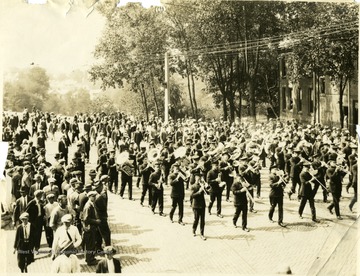 Marching band in uniform marches down a brick street with people watching from the sides.