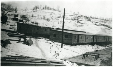 Two complete barracks and one incomplete barracks with piles of lumber stacked nearby.