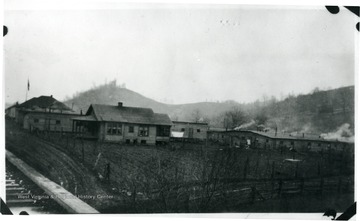 Barracks and houses with field beside and a flag on a pole to the left.