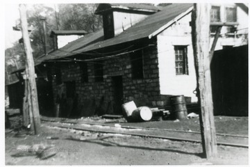 Barrels are sitting outside next to the house and the tracks beside the power house.