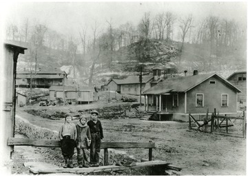 Three boys standing in front of houses.