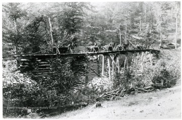 Mules hauling carts across a wooden bridge.