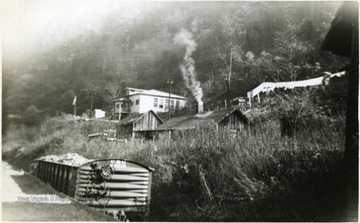 Clothes are hanging on the line behind building with smoking chimney.