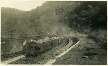 Smoke rises from the coke ovens. Filled coal cars are next to them.