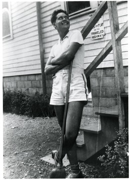 Man leaning against a porch railing holding a broom.