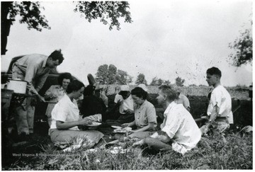 Friends each lunch on the ground outside of a garden.