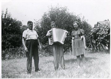 The Viola family standing in the grass with Tullio holding a accordion.