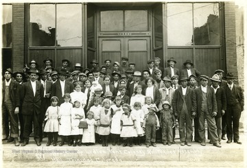 Group portrait of men, women, and children standing out front of an assembly hall.