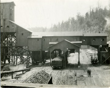 Coal car under a tipple.  Men with horse drawn carriage also going under the tipple.