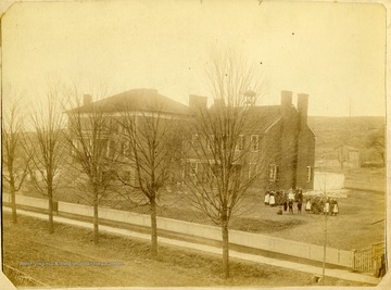 A group of people stand outside of a large brick building.