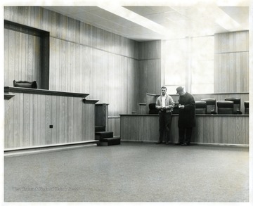 Two men are standing in a redecorated Monongalia County Courtroom in the Courthouse in Morgantown, West Virginia.