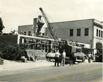 Construction on public library. Workers can be seen on the road on and the building. 