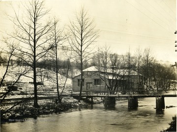 Glass company located in Morgantown, W. Va., bridge runs across the river to factory. Snow laying on ground. Trees are bare. 