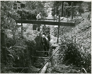 Two men digging in a deep ditch while another is watching, Morgantown, W. Va.