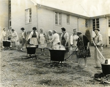 Men and women stir apple butter in large kettles over fires on the lawn of a Morgantown church.