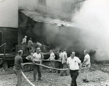 Men hold the water hose for the firefighters, as they try to extinguish a fire at the Davis-Lynch Glass Company in Star City, near Morgantown, W. Va. 