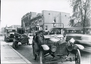 'Two beat up old automobiles with Indiana license plates are parked at the corner of High Street and Kirk Street' in Morgantown, W. Va. One bears a sign which reads 'I may be old but I can still get hot.  Behind the automobiles, Richard Restaurant can be seen. 