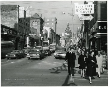 People walking in the crosswalk as cars are stopped at a red light.  Christmas decorations are on the lamp posts, Morgantown, W. Va.