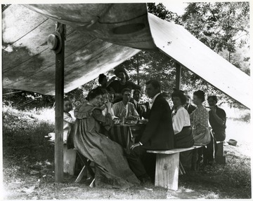 Group of men and women seated around a wooden table eating.