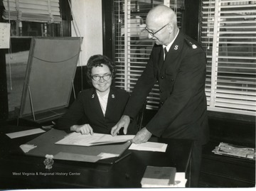 A man and woman who are working for the Salvation Army are discussing something from a book.