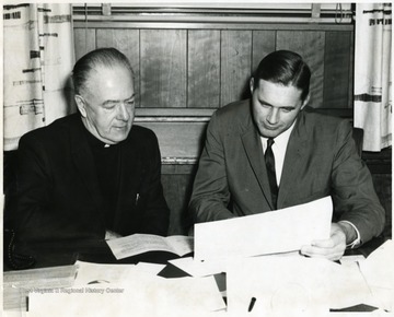 Father Mueller sits with another man looking over documents. 