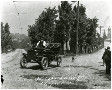 Old automobile seen at the corner of Front Street and Beechurst. Dog is chasing car. 