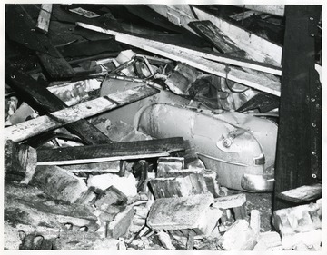 Back end of a car visible in the rubble of a collapsed building.