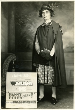 Man dressed as Fanny Foley next to a sign advertising a Halloween appearance at the Warner Theater.