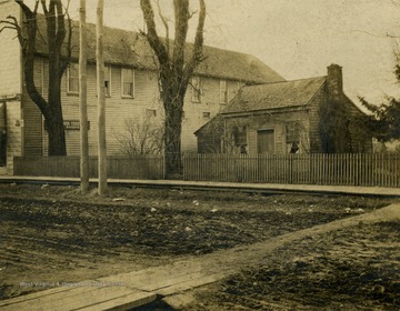 Small, dilapidated, wooden house beside what appears to be a shoe factory or store.