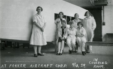 A group of women workers sitting on a bench and standing by their project at the Fokker Aircraft Corp.