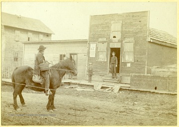 Man seated on a horse looking towards the Burke and Summers building in Montrose, W. Va.  Williah H. Burke standing in door.  Boy standing on sidewalk in front of building.