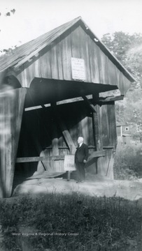 View of man standing at entrance of bridge next to 'closed bridge' sign.