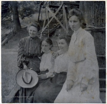 A group of unidentified women gathered outside in front of a tree.