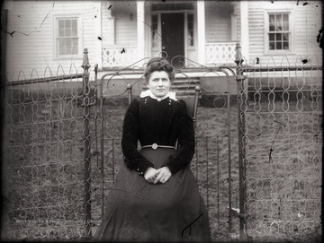 A portrait of seated woman by the wire fence taken outdoors.