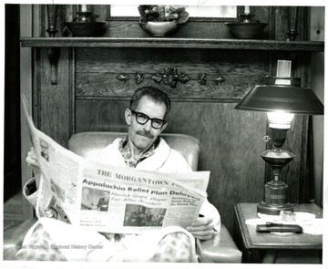 An unidentified man sits in couch with papers in his hands.