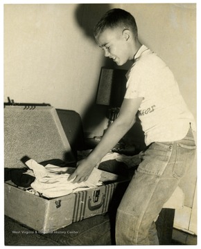 An unidentified boy reaches to an opened trunk filled with clothes.