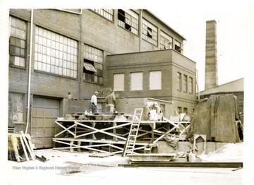 Workers working on a new addition to the front of the building at Adamston Flat Glass; a small tank stack in the background.